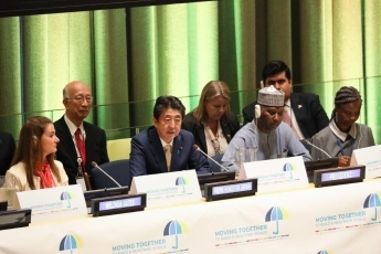 Group of individuals sat at white table. There is a large green curtain behind.