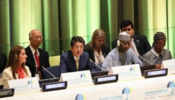 Group of individuals sat at white table. There is a large green curtain behind.